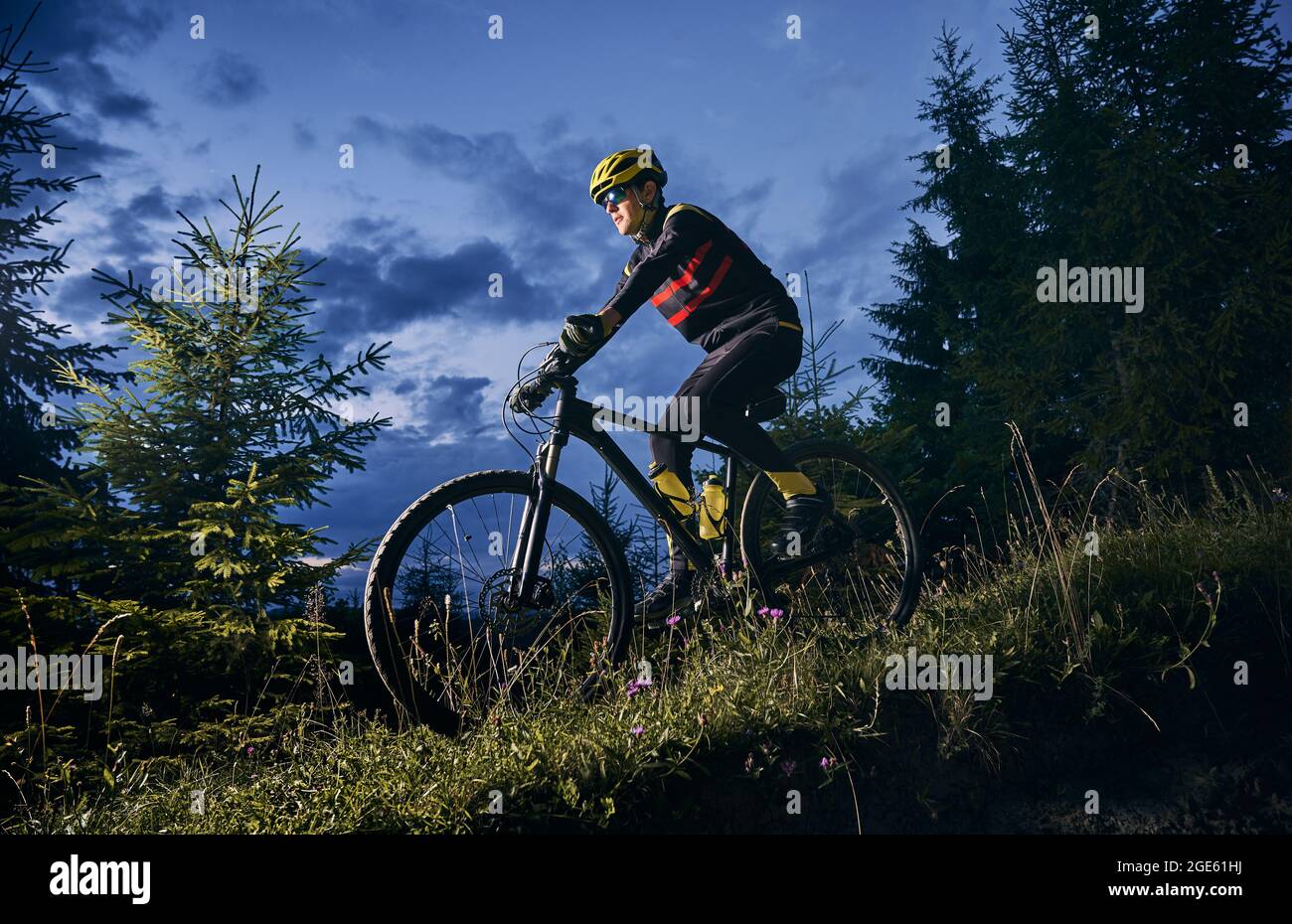 completar después de esto asiático Joven montando en bicicleta cuesta abajo con hermoso cielo azul por la  noche en el fondo. Hombre ciclista en deportes de ciclismo traje ciclismo  por la colina de hierba por la noche.