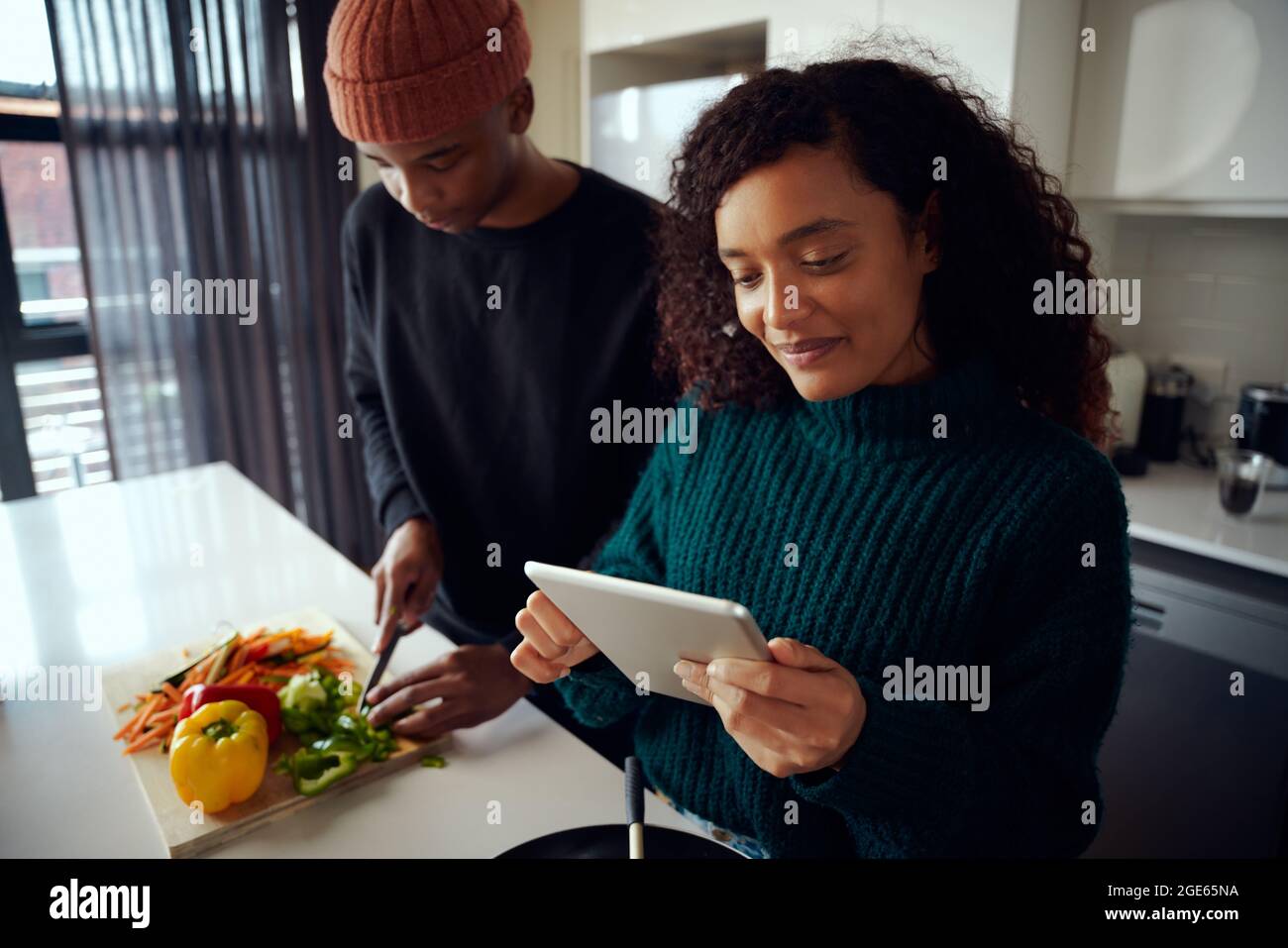Joven pareja mixta de carreras cocinando comida en la cocina y usando una tableta. Mujer mirando la tableta para la receta del alimento. Fotografías de alta calidad Foto de stock