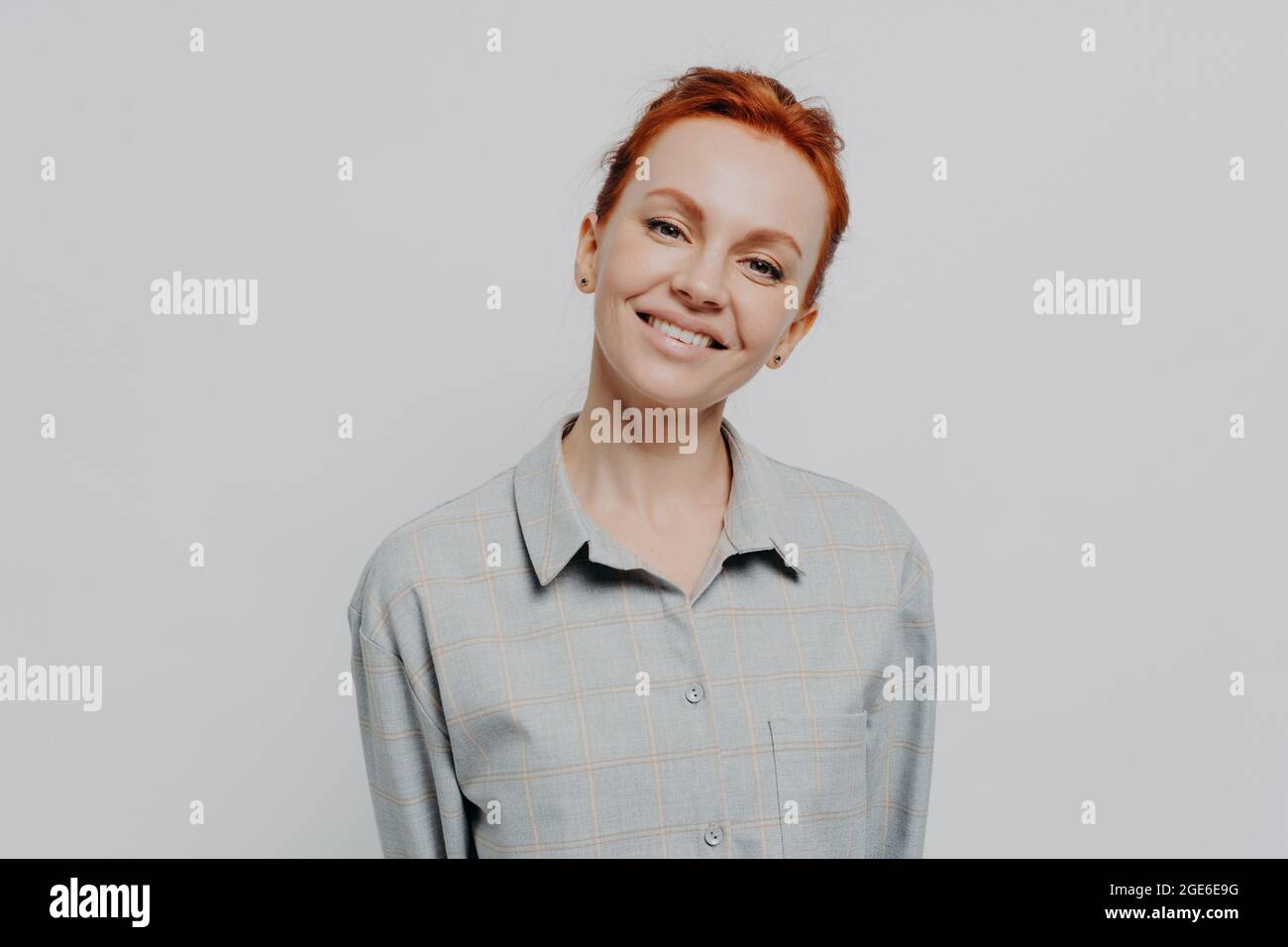 Alegre hermosa mujer de pelo rojo con una sonrisa radiante posando aislado en el fondo gris del estudio Foto de stock