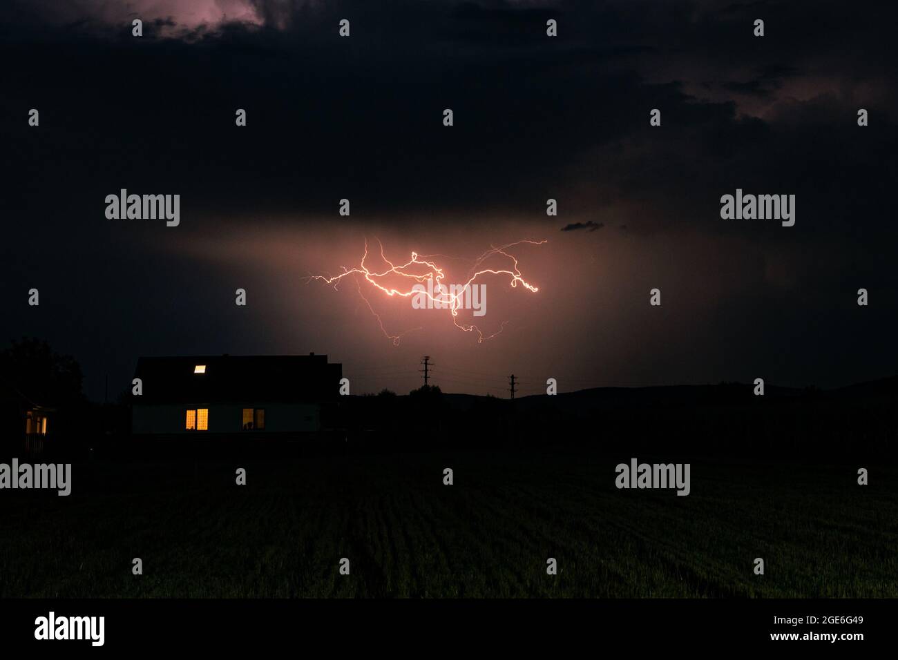 Un rayo sobre una casa se regatea a través del cielo durante una fuerte tormenta eléctrica Foto de stock