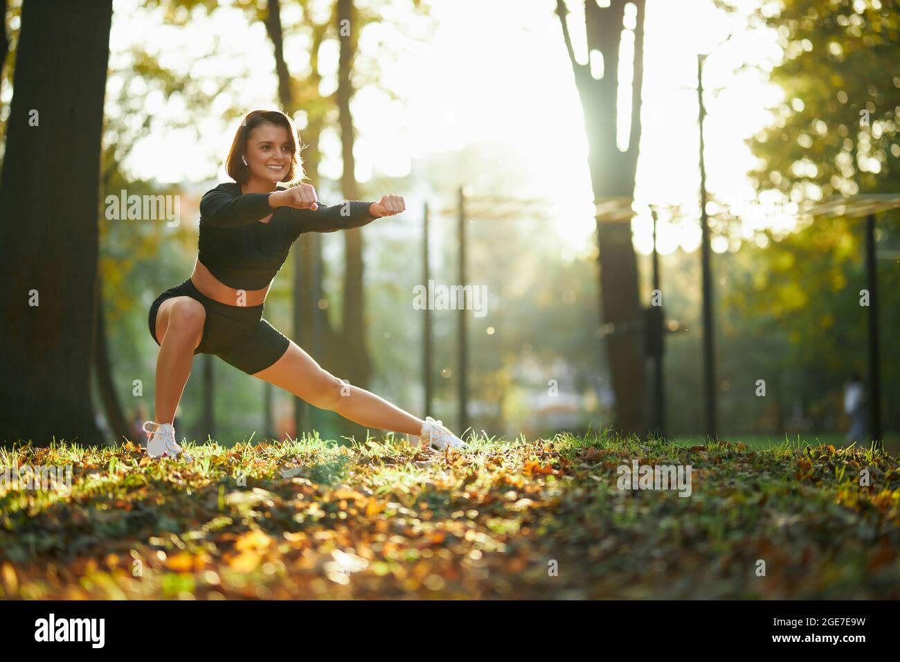 Mujer joven deportiva en activewear practicando en forma física durante el día soleado al aire libre. Mujer feliz con pelo marrón disfrutando de un estilo de vida activo y saludable en el aire fresco. Foto de stock