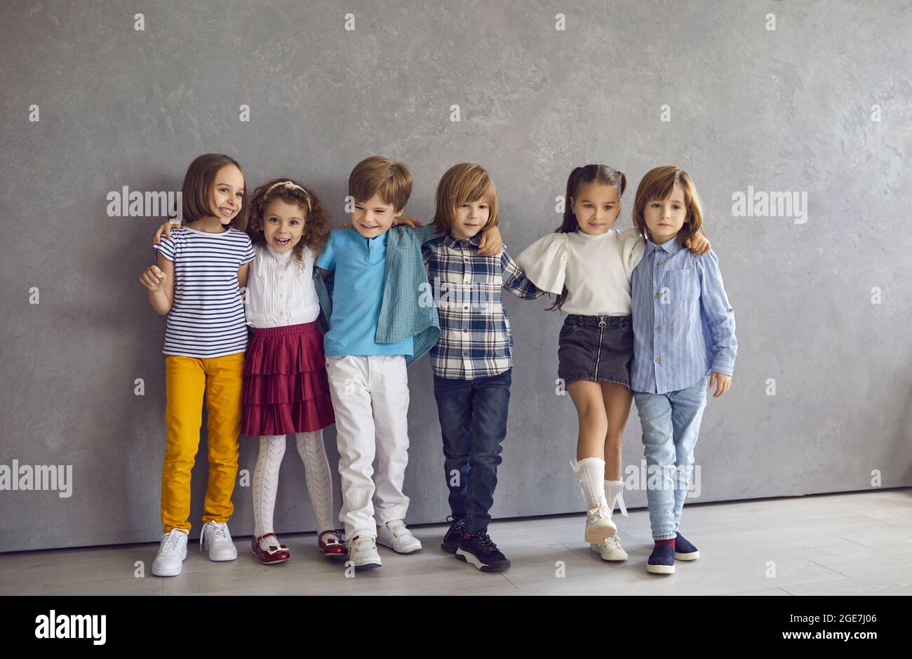 Retrato de niños y niñas que se divierten juntos de pie contra el telón de fondo de una pared gris. Foto de stock