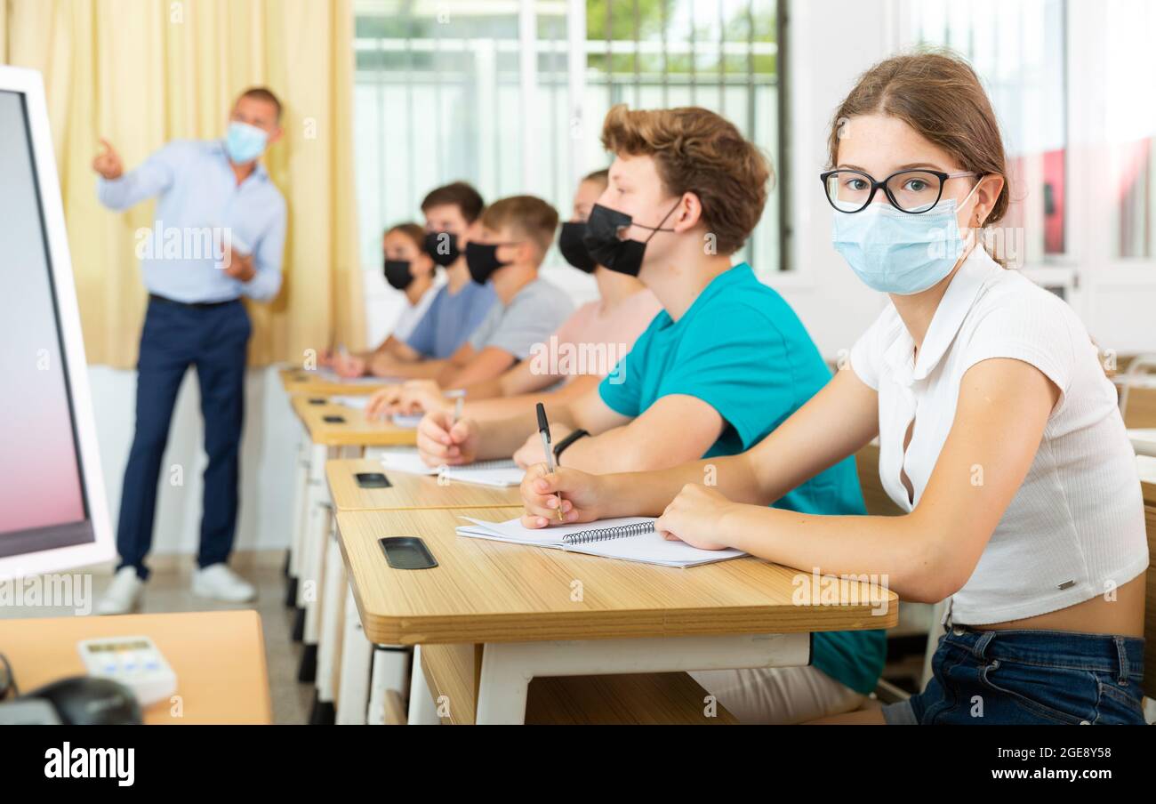 Adolescente en máscara protectora estudiando en la universidad con compañeros de clase Foto de stock