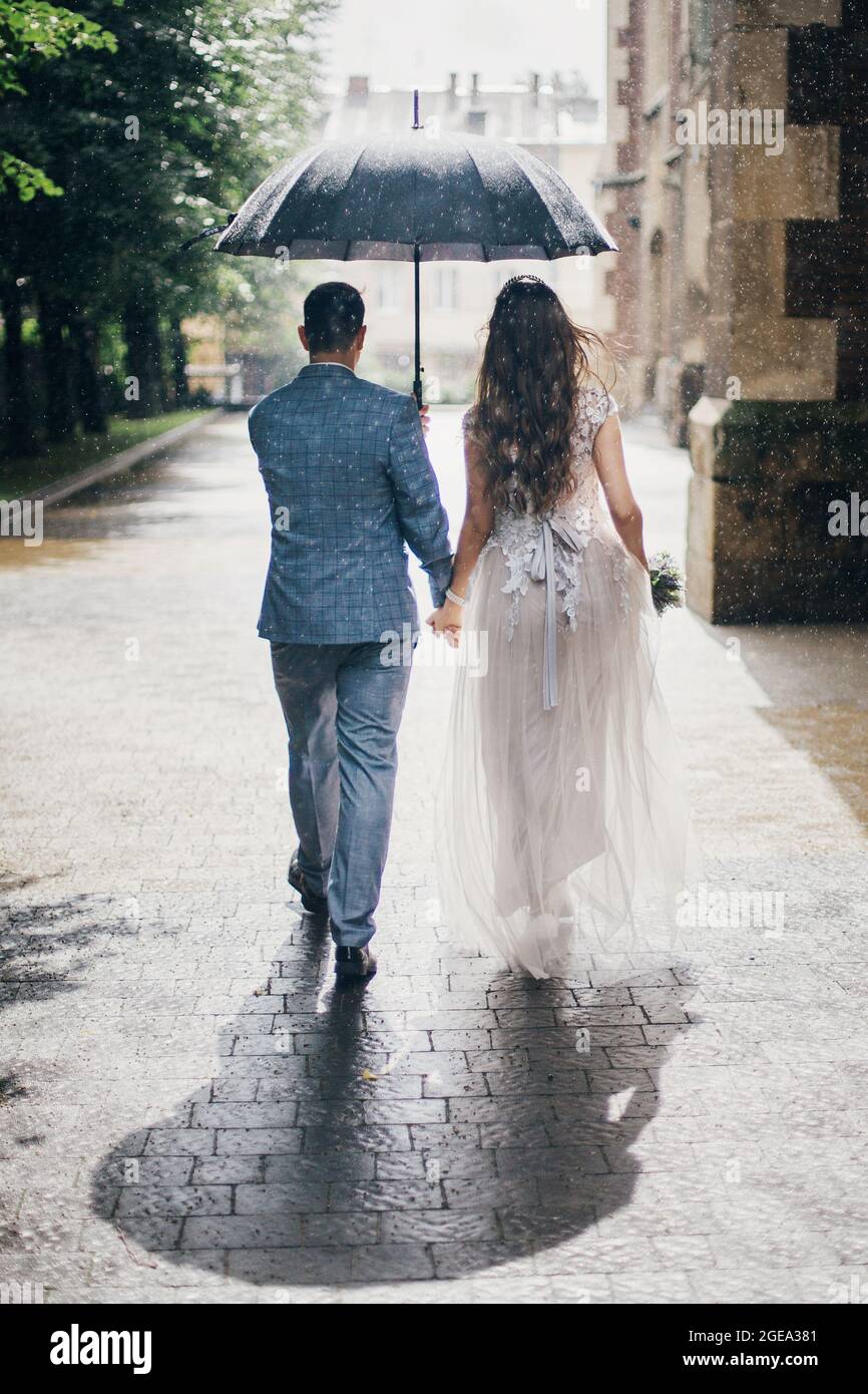 Novia y novio con caminando bajo paraguas y sujetando las manos sobre el fondo de la vieja iglesia bajo la lluvia. Provenza boda. Hermosa boda pareja walki Fotografía stock -