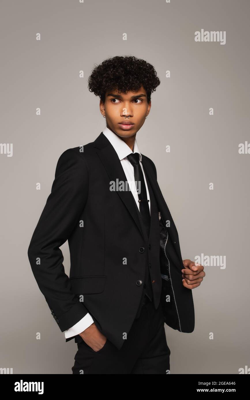 hombre afroamericano de ropa formal negra mirando hacia fuera mientras  sujeta la mano en el bolsillo aislado en gris Fotografía de stock - Alamy