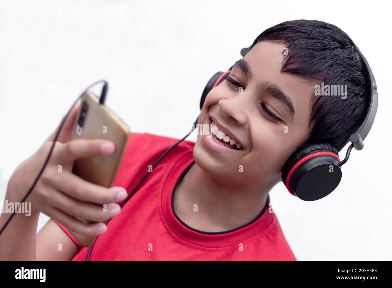 Lindo niño sonriendo cara escuchando música con auriculares y móvil sobre fondo blanco aislado. Foto de stock