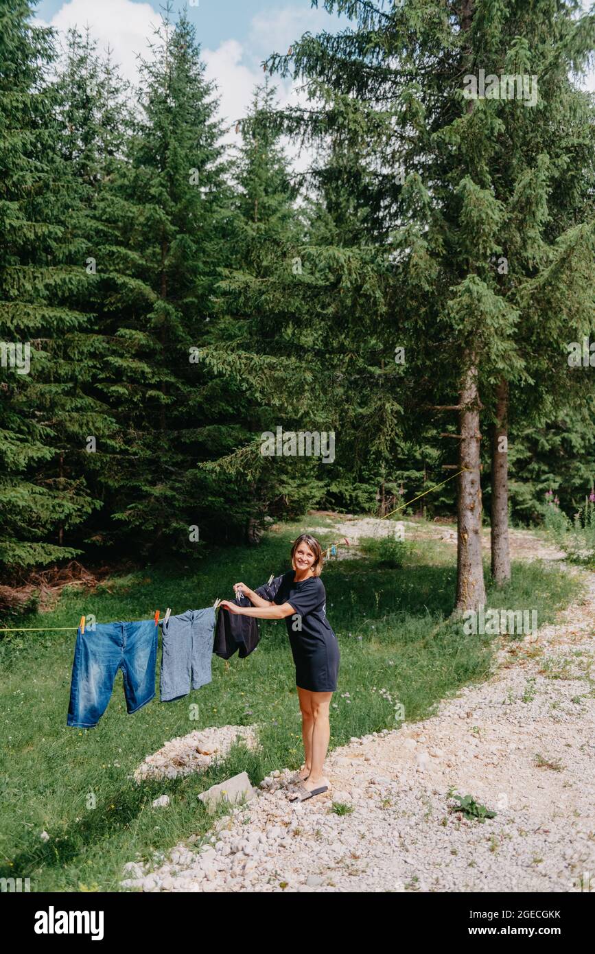 Mujer joven cuelga ropa en la línea de ropa al aire libre en el patio de  una casa de campo de pueblo, verano y concepto de frescura, día de lavado.  Chica linda