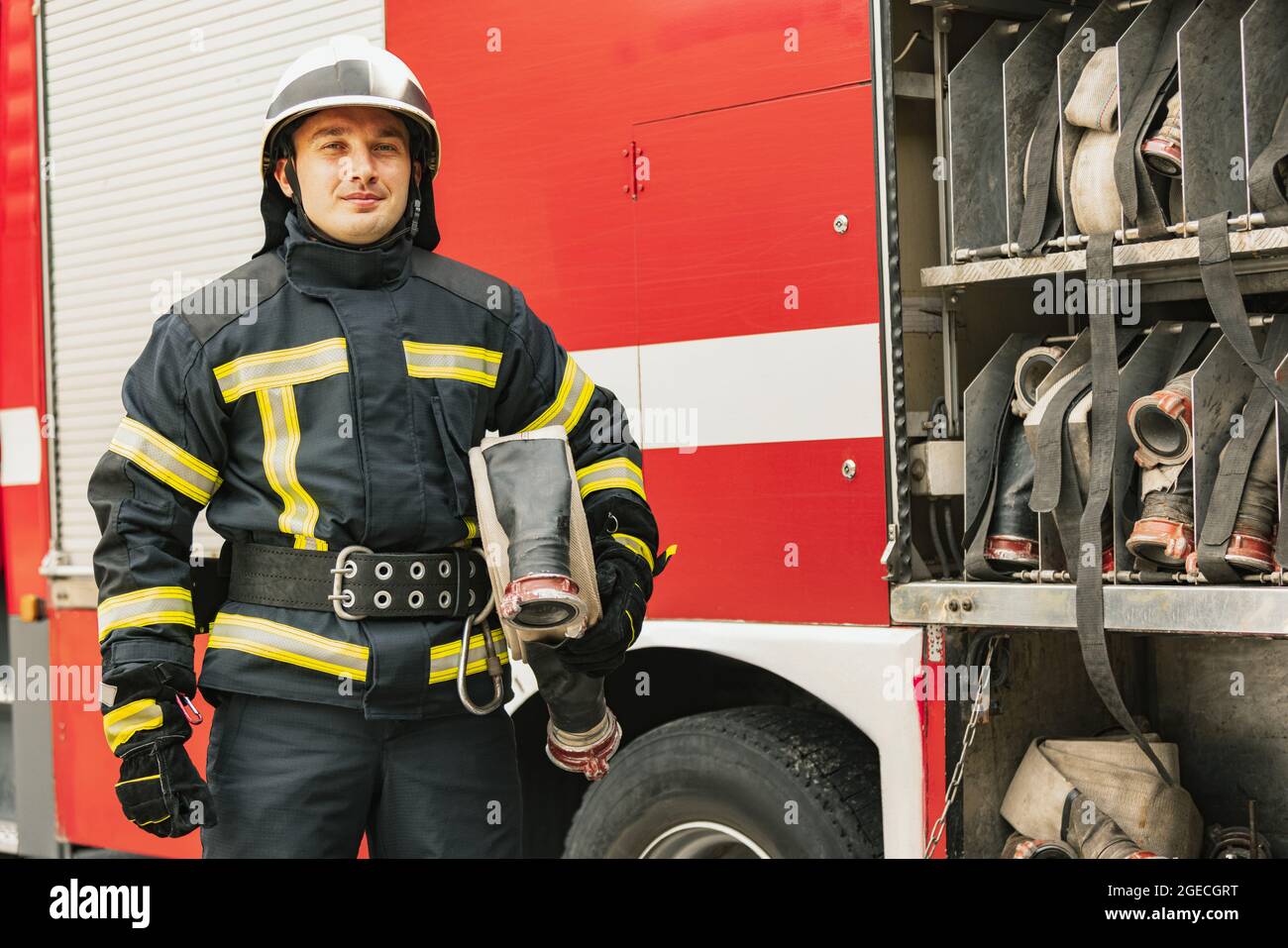 Un joven bombero masculino vestido con uniforme con manguera de agua en un  camión de bomberos listo para su despliegue Fotografía de stock - Alamy