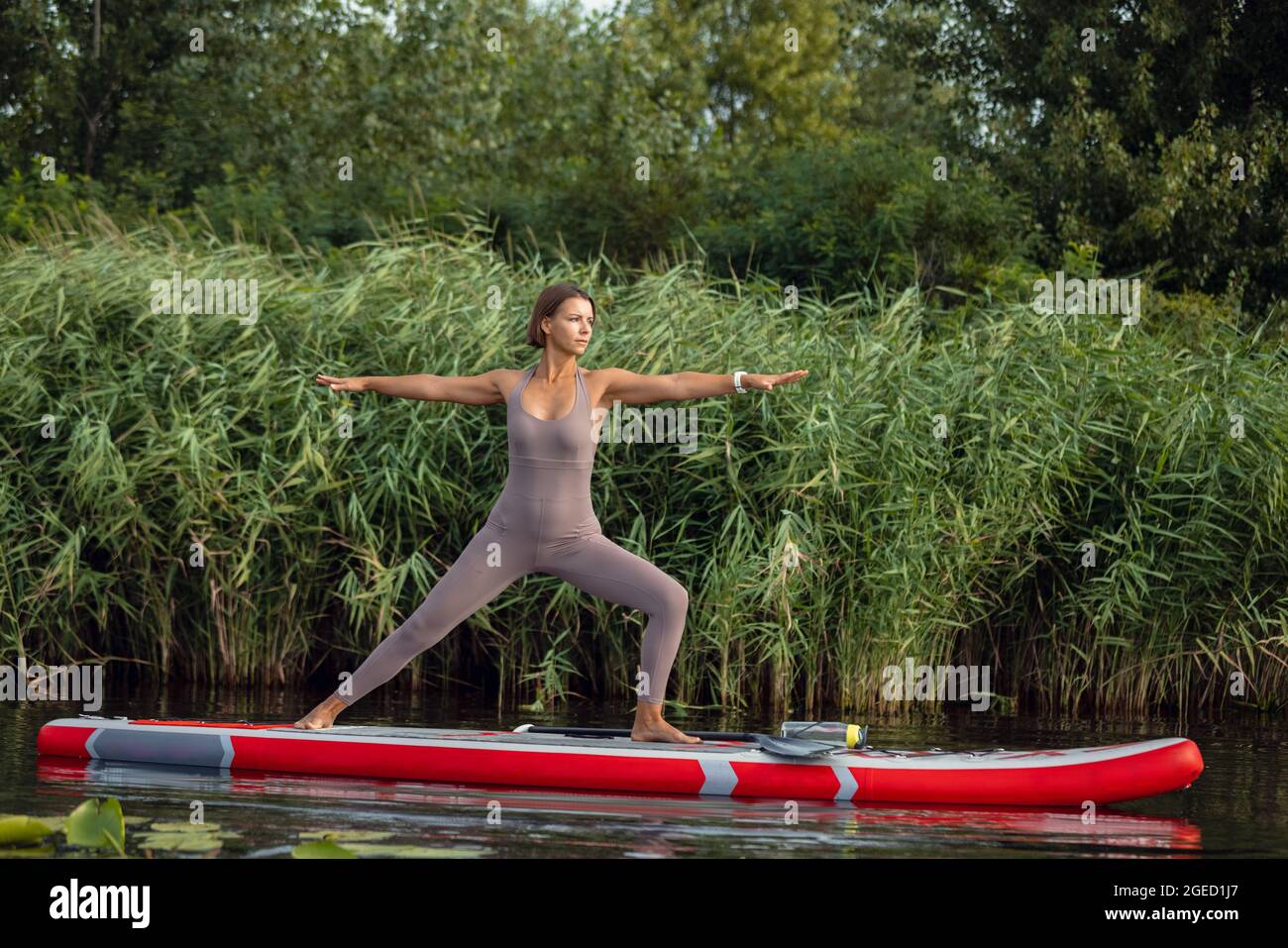 Una joven caucásica hermosa chica delgada haciendo yoga, pilates en tabla de paddle, SUP solo en la mañana de verano. Concepto de vida activa, deporte, actividad de ocio Foto de stock