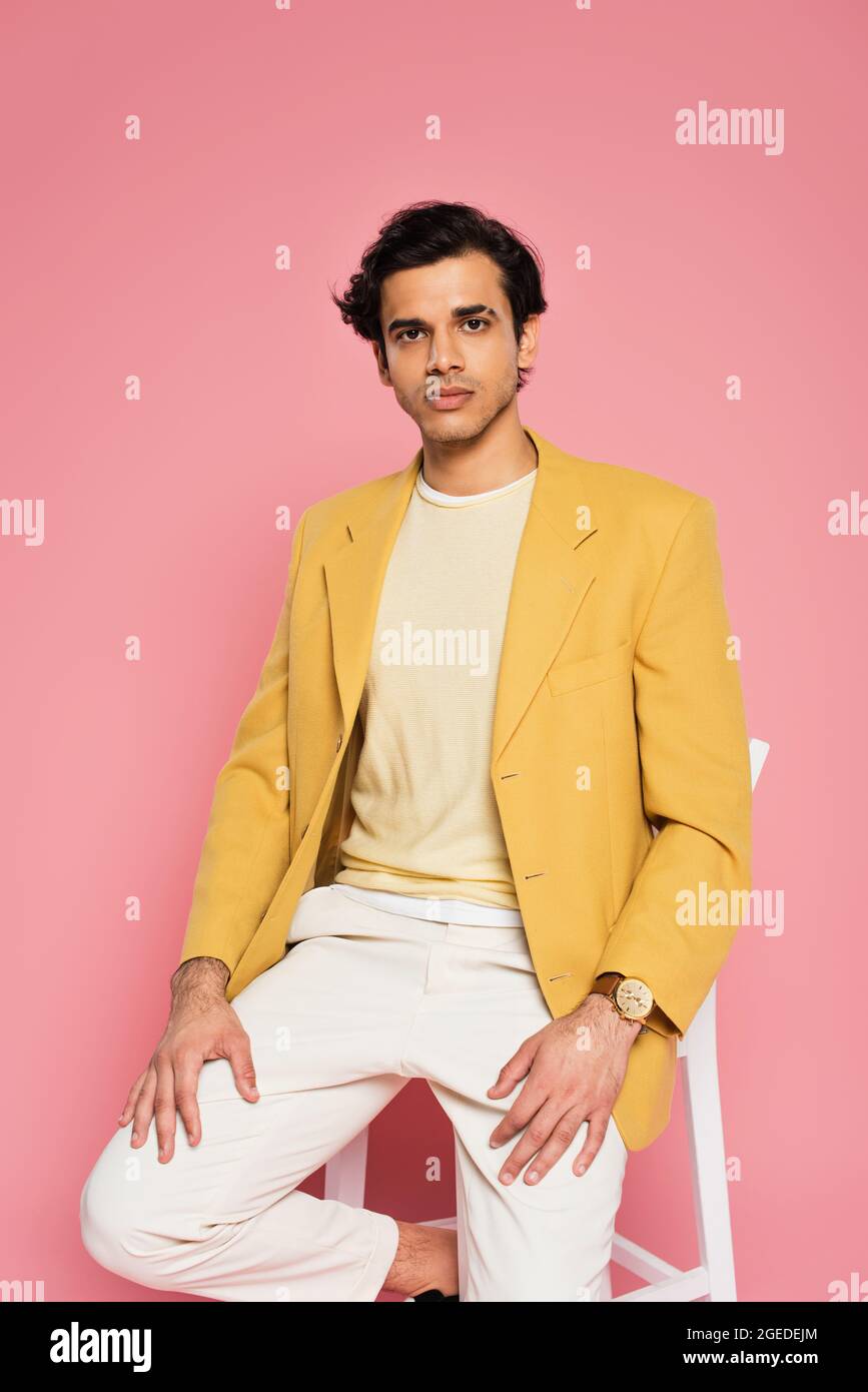 hombre joven en blazer amarillo sentado en silla blanca aislado en rosa Fotografía de Alamy