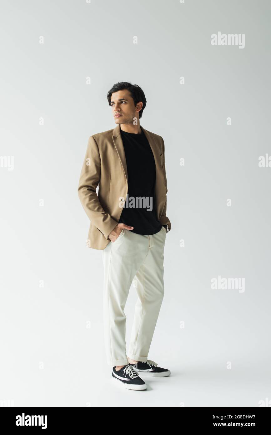 largo de hombre joven en un elegante blazer beige de pie con las manos en  los bolsillos en gris Fotografía de stock - Alamy