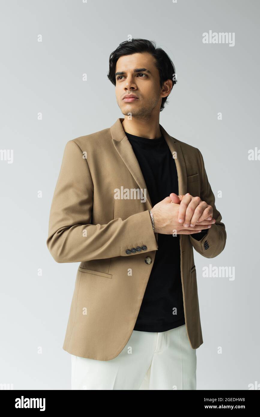 hombre joven en un elegante blazer que se ve aislado en gris de stock -