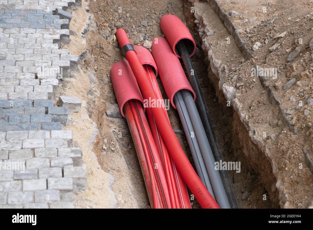 El tubo corrugado rojo está enterrado bajo tierra en la calle hecho para la  instalación de infraestructura de cable eléctrico. Sitio de construcción  con Una gran cantidad de suministro e Fotografía de