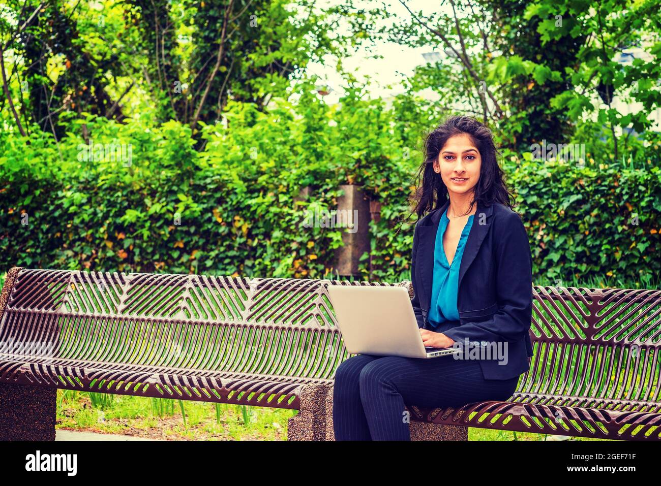 Mujer joven india con una camisa azul y blazer negro sentado en el parque  con un ordenador portátil Fotografía de stock - Alamy