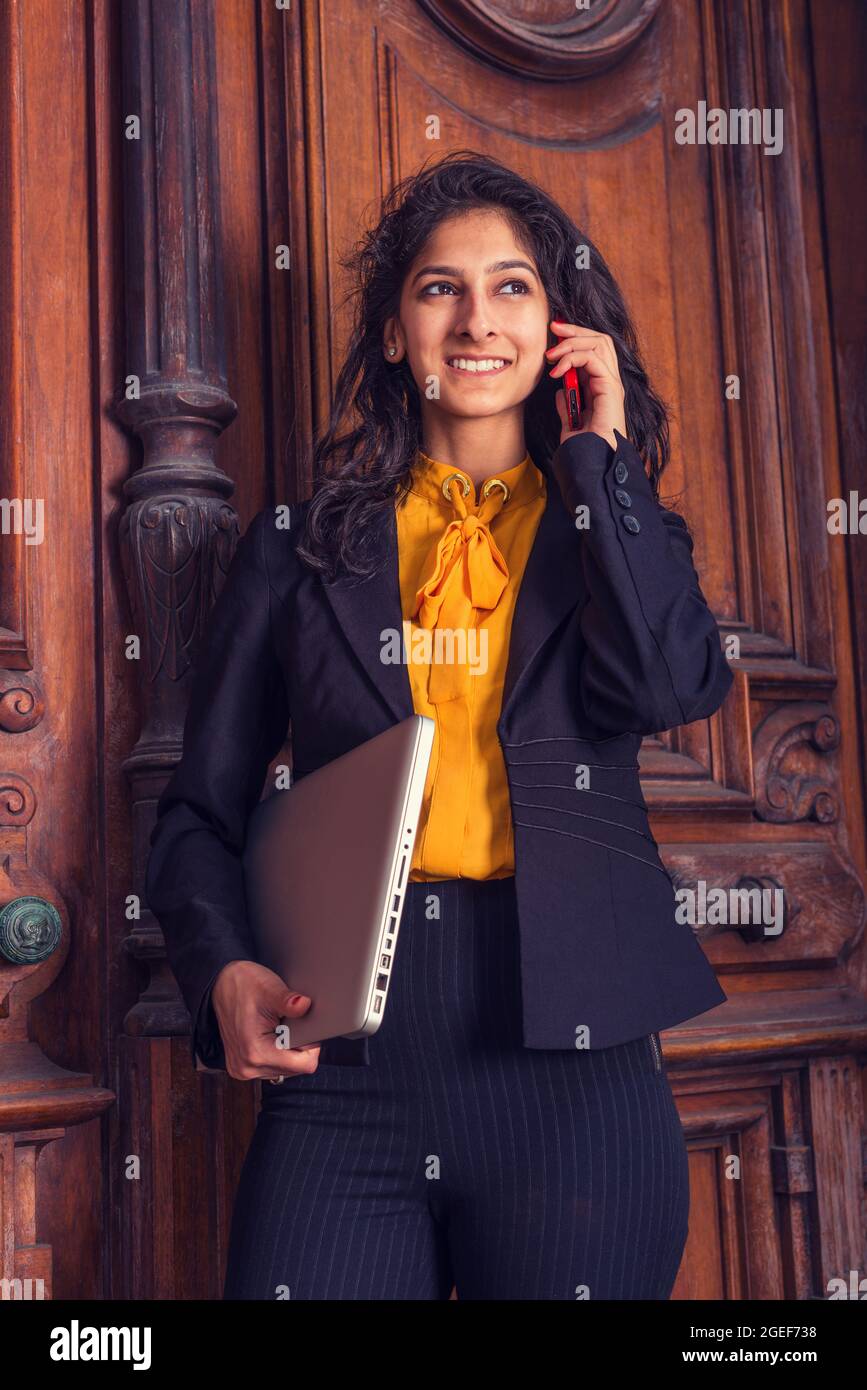 Tiro vertical de una mujer india con una camisa naranja y un blazer con un  ordenador portátil en su mano Fotografía de stock - Alamy