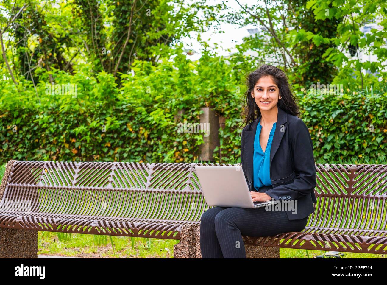 Mujer joven india con una camisa azul y blazer negro sentado en el parque  con un ordenador portátil Fotografía de stock - Alamy