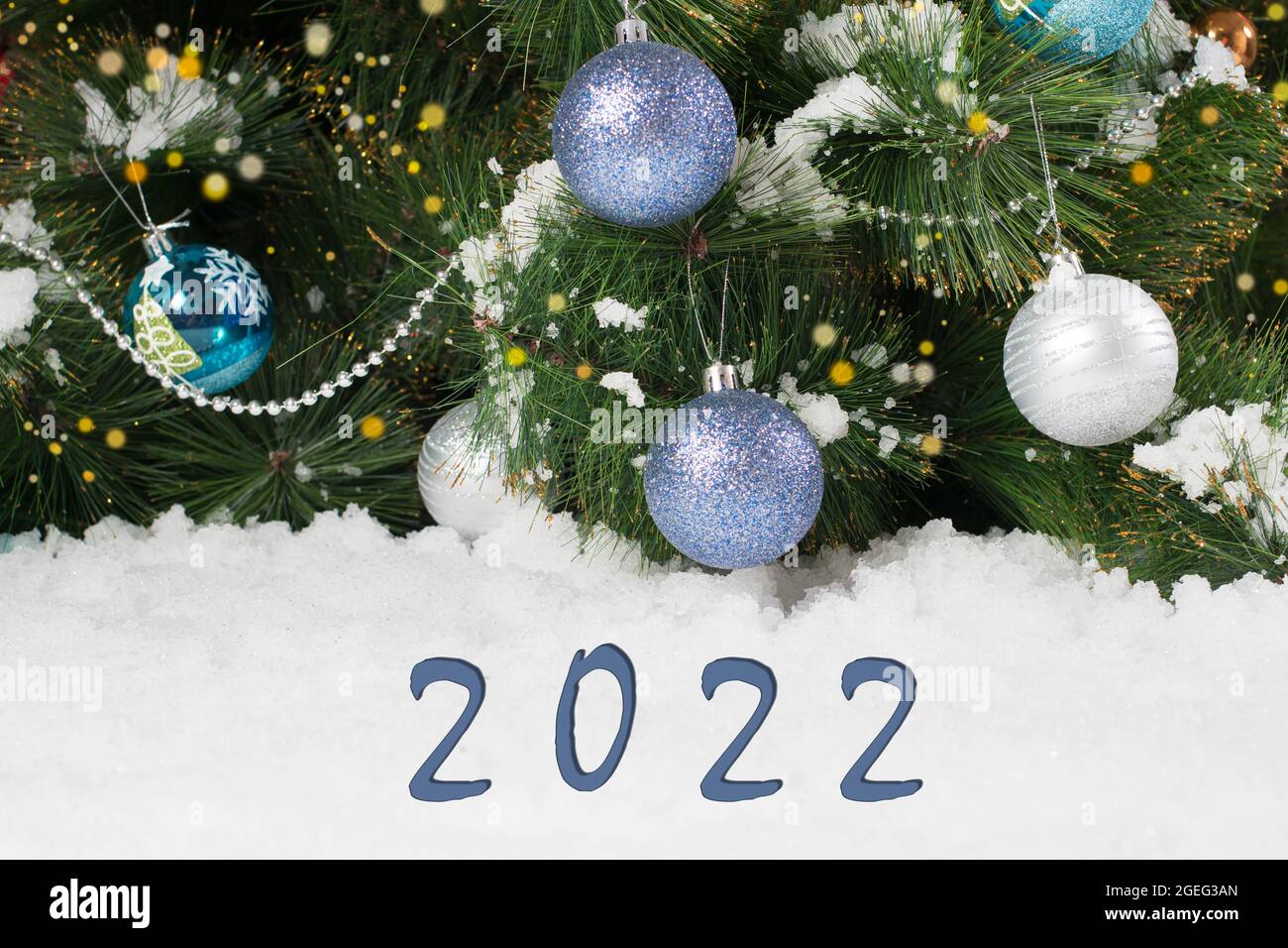 Hermosa postal navideña horizontal en azul y blanco con números 2022 - árbol con bolas de juguetes y nieve Foto de stock