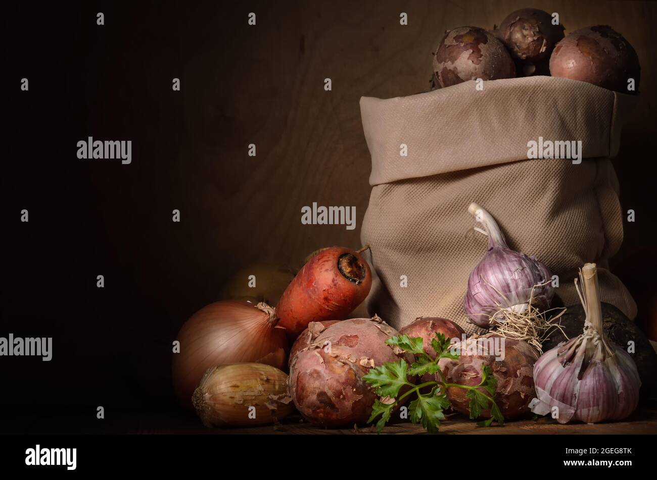 patatas en una bolsa de tela y otras verduras en un estilo rústico sobre un fondo de madera oscura Foto de stock