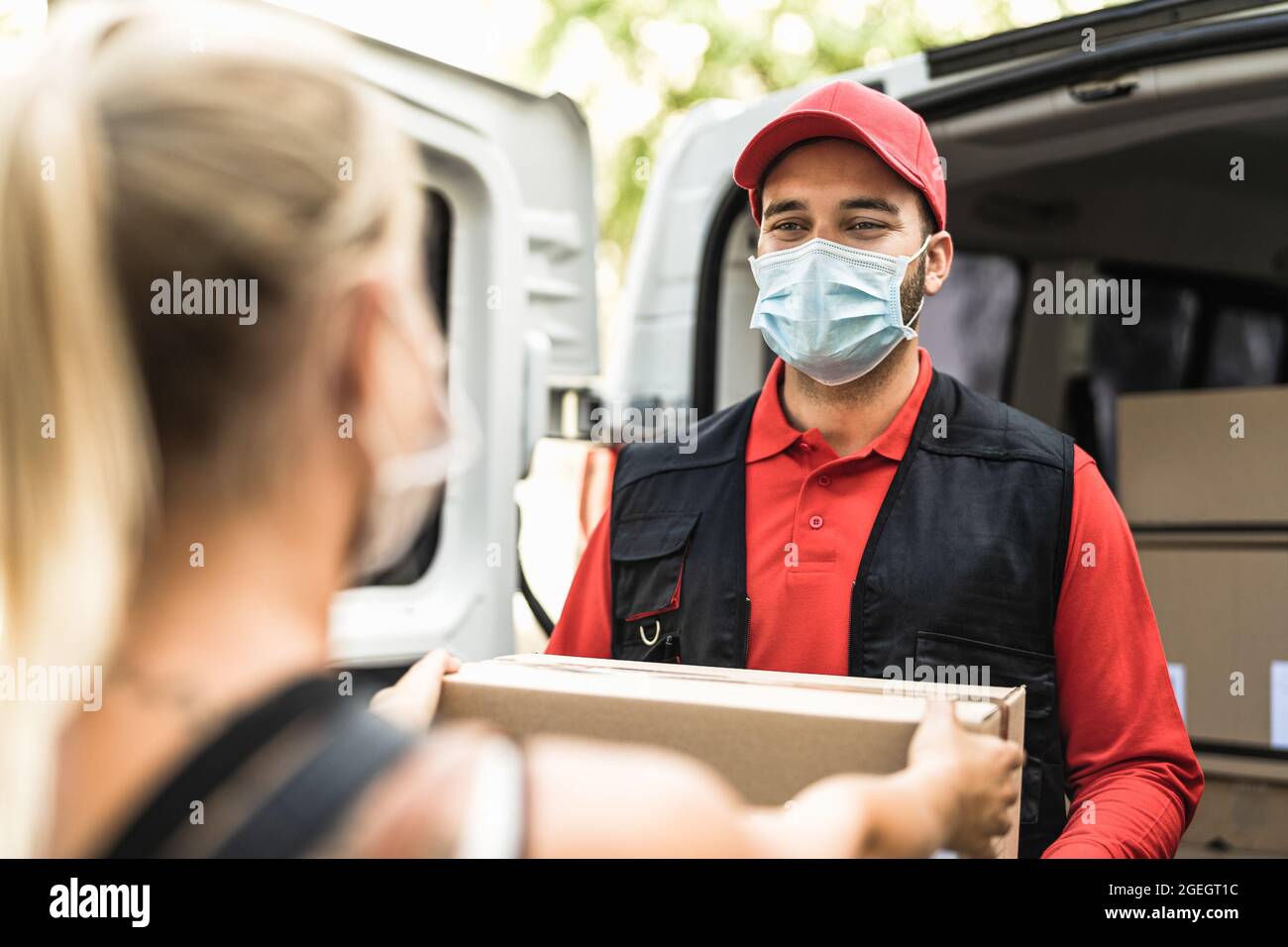 Hombre de entrega en el trabajo con máscara facial - Mujer joven que recibe un pedido en línea del mensajero expreso Foto de stock