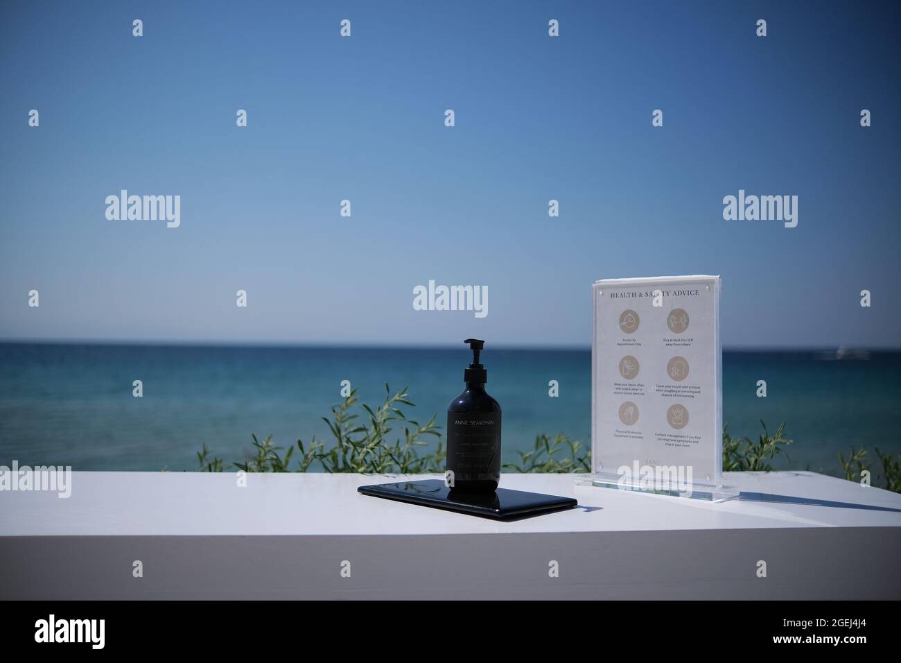 Sani, Grecia - 16 de agosto de 2021 : Un gel antiséptico de handrub a base de alcohol y un formulario de consejos de salud y seguridad frente al mar egeo Foto de stock