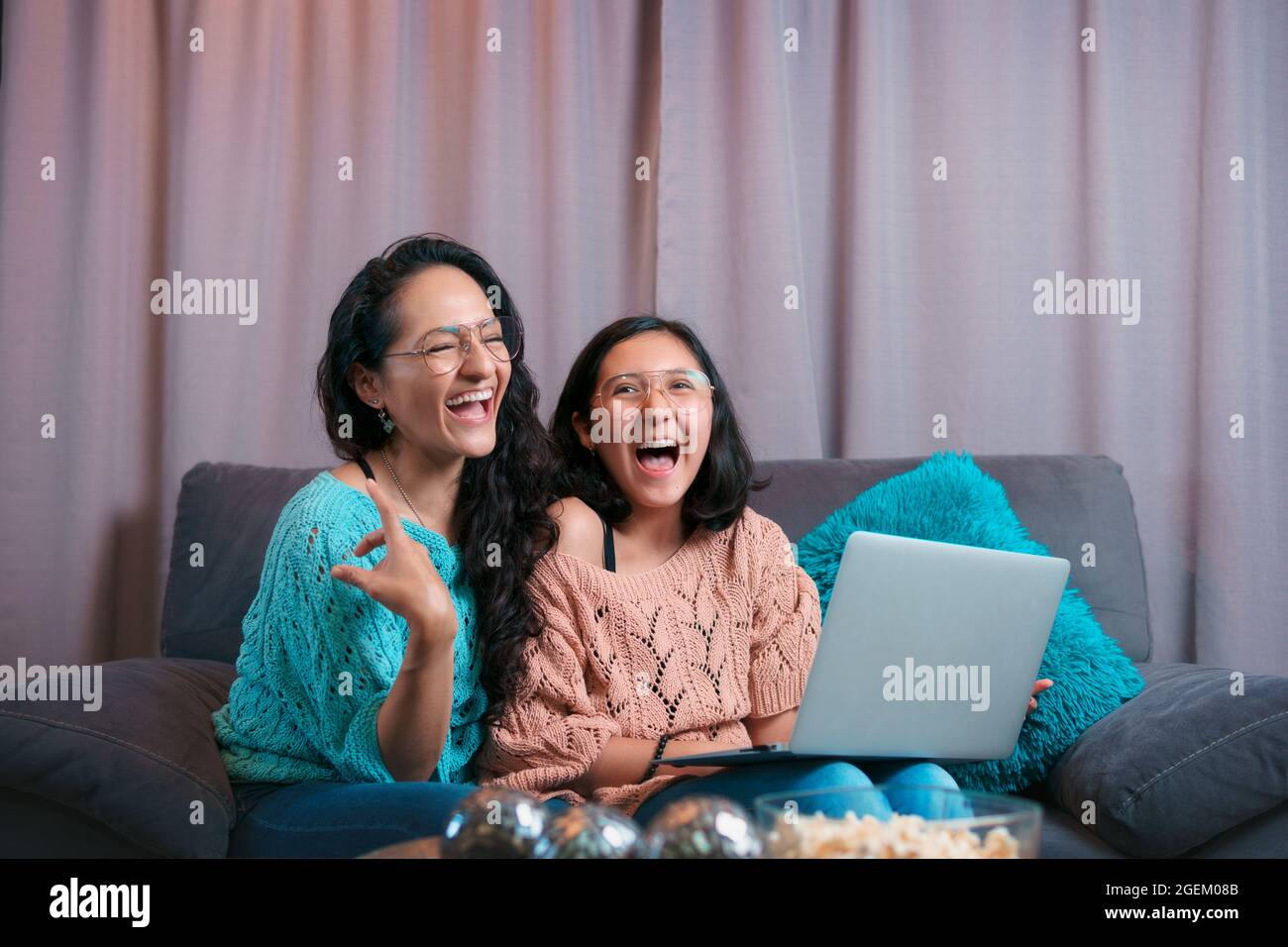 Vista horizontal de una madre y una hija usando un portátil, ambos riendo en voz alta por lo que han visto en la pantalla de la computadora Foto de stock