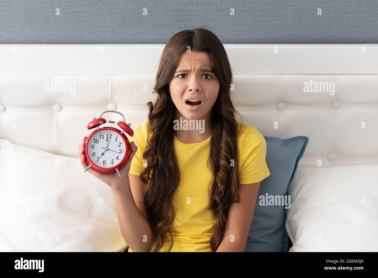 Una niña preocupada que sostiene el reloj despertador que se molesta con  dormir demasiado tarde por la mañana Fotografía de stock - Alamy
