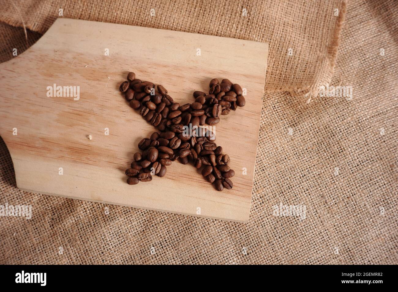 granos de café en forma de cruz sobre una tabla de corte de madera sobre un fondo de madrigueras. concepto minimalista de fotos de comida o bebida para materiales de diseño, escritura Foto de stock