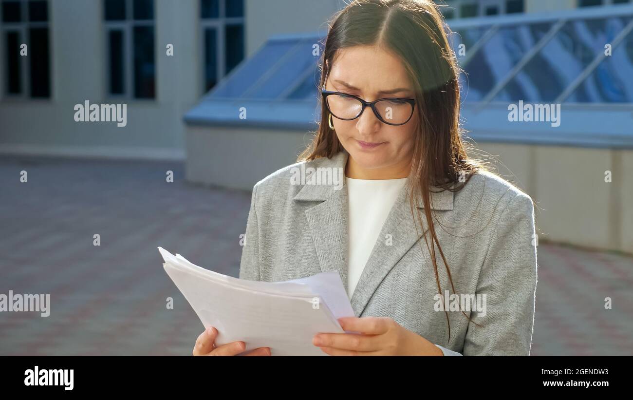una mujer joven con un traje formal y gafas con una cara seria examina los  documentos en la calle Fotografía de stock - Alamy