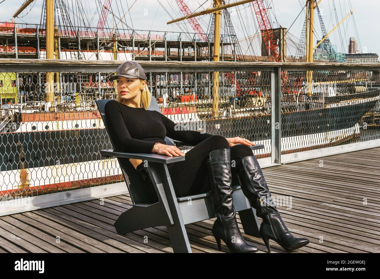Mujer con una gorra de cuero negro, pantalones, botas largas, sentada en la  silla en la terraza en el puerto Fotografía de stock - Alamy