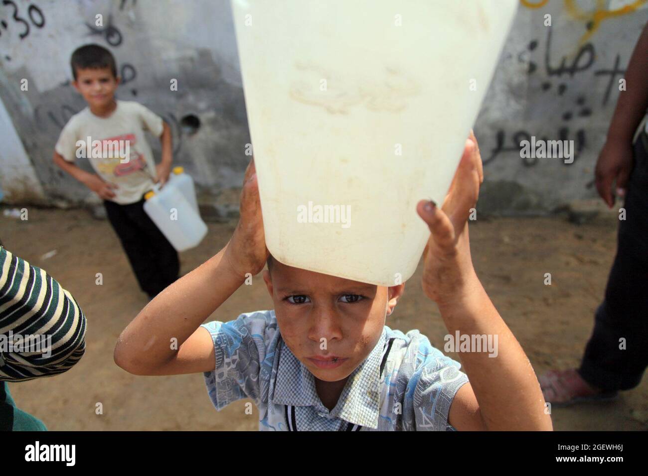 Retrato de un niño palestino que lleva una lata de agua sobre su cabeza. Ciudad de Gaza. Foto de stock