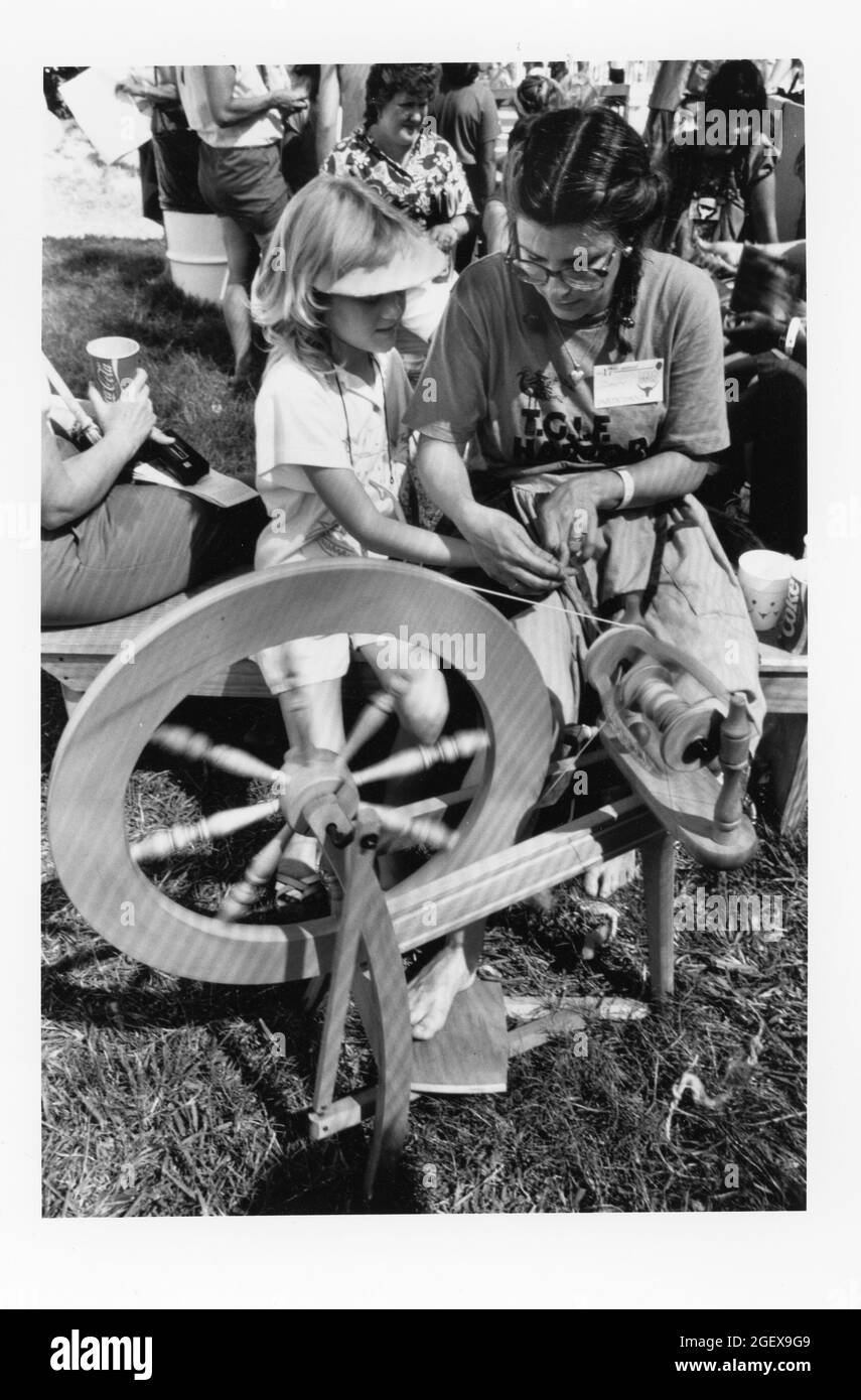San Antonio Texas USA, alrededor de 1989: Una joven que aprende sobre hilar lana en una rueda de hilado a la antigua usanza de un experimentado voluntario en el Festival de Texas Folklife. ©Bob Daemmrich Foto de stock