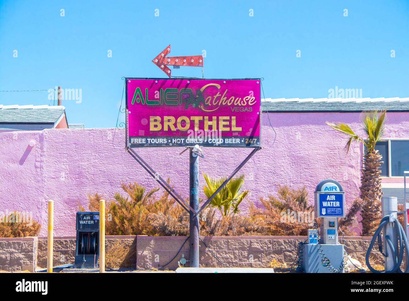 5-25-2021 Las Vegas USA - Identifícate en el burdel desierto de la cátara Alien con flecha de neón en frente de un edificio de estuco rosa con palmeras, coches y agua Foto de stock