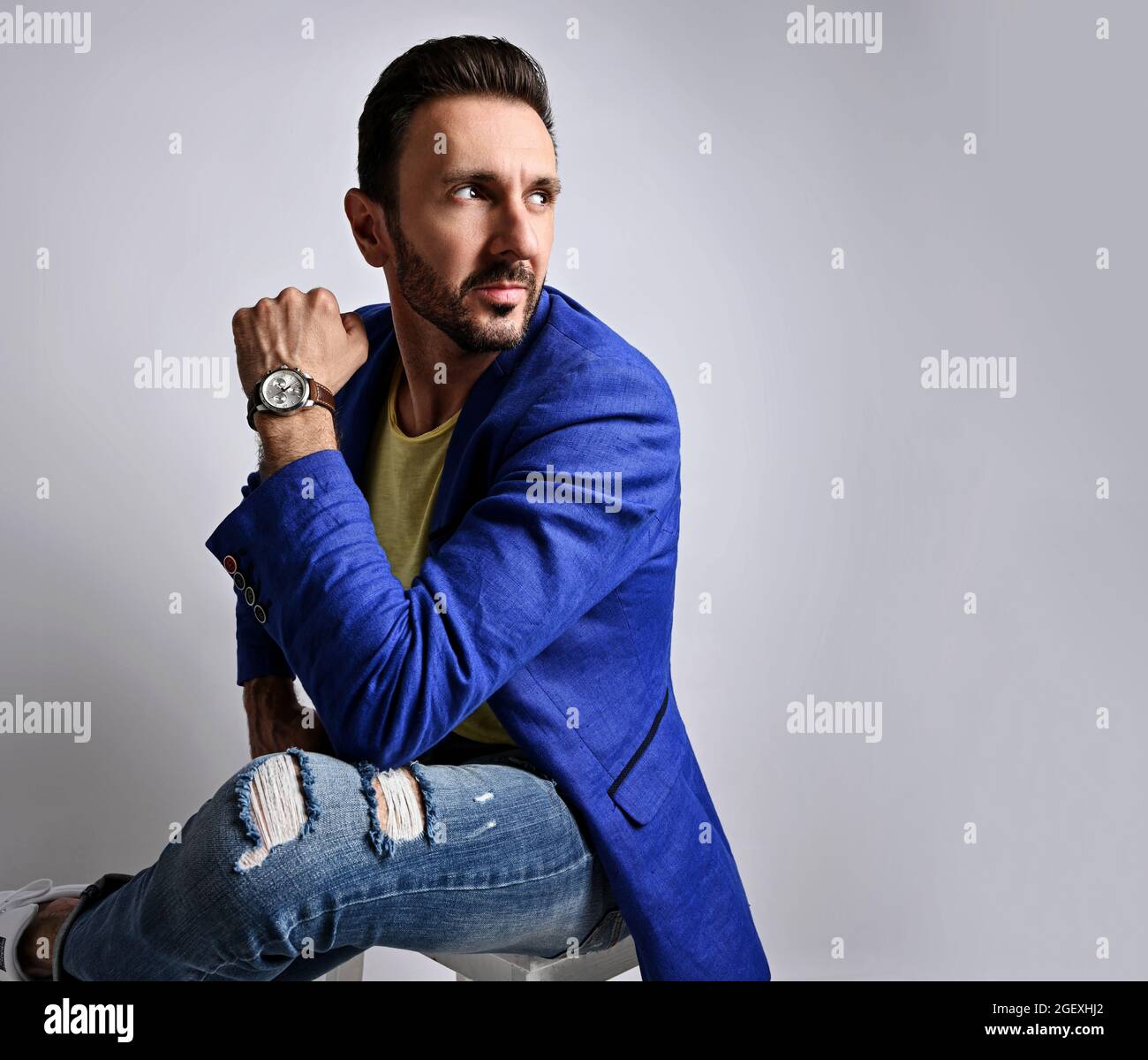 Retrato hombre maduro sin afeitarse modernos jeans rasgados y chaqueta azul sentado en el taburete mirando el espacio de copia detrás de él Fotografía de stock - Alamy