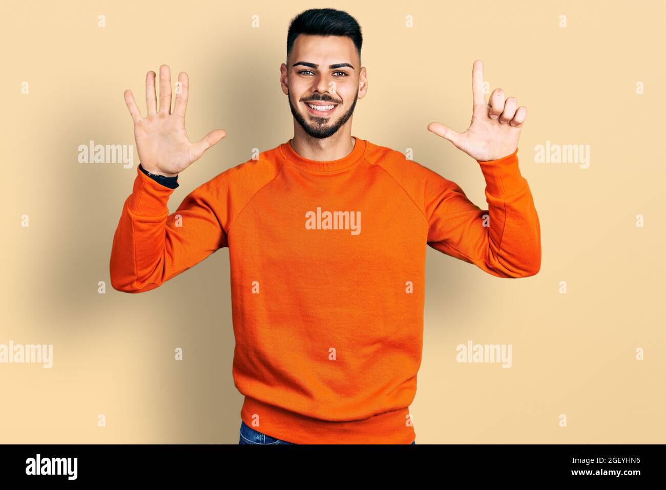 Joven hombre hispano con barba con suéter naranja informal mostrando y  apuntando con los dedos número siete mientras sonriendo con confianza y  feliz Fotografía de stock - Alamy