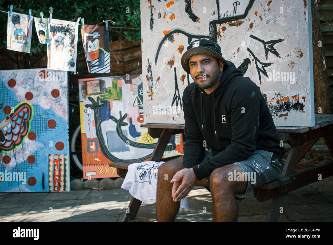 Joven artista masculino sentado frente a su pintura en un estudio al aire libre. Foto de stock