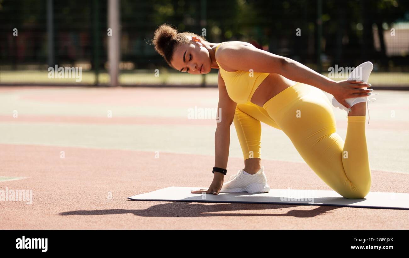 Mujer deportiva negra en la pierna de estira de ropa deportiva amarilla  Fotografía de stock - Alamy