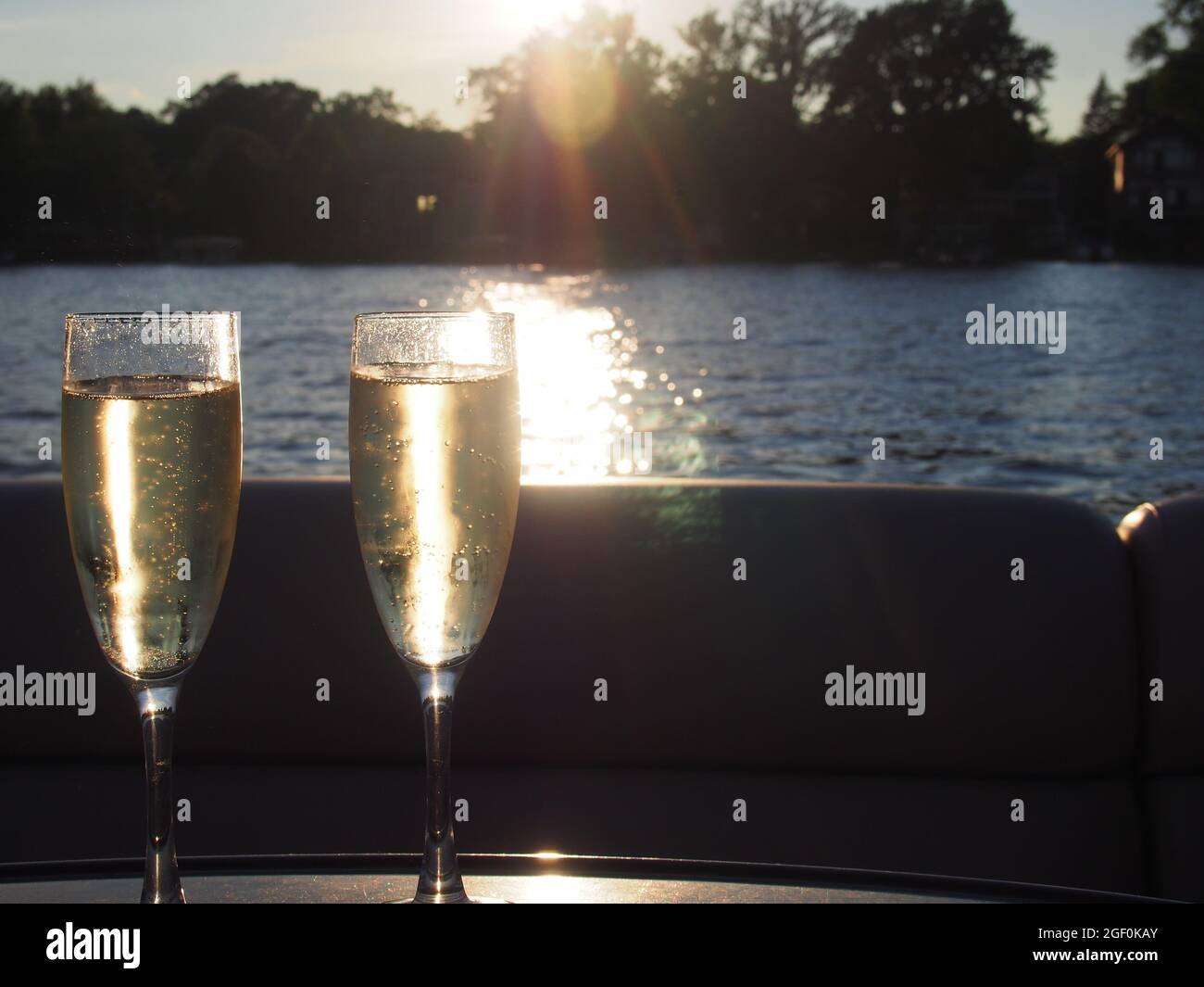 Tostada con champán y burbujas con luz solar contra una puesta de sol en el lago Foto de stock
