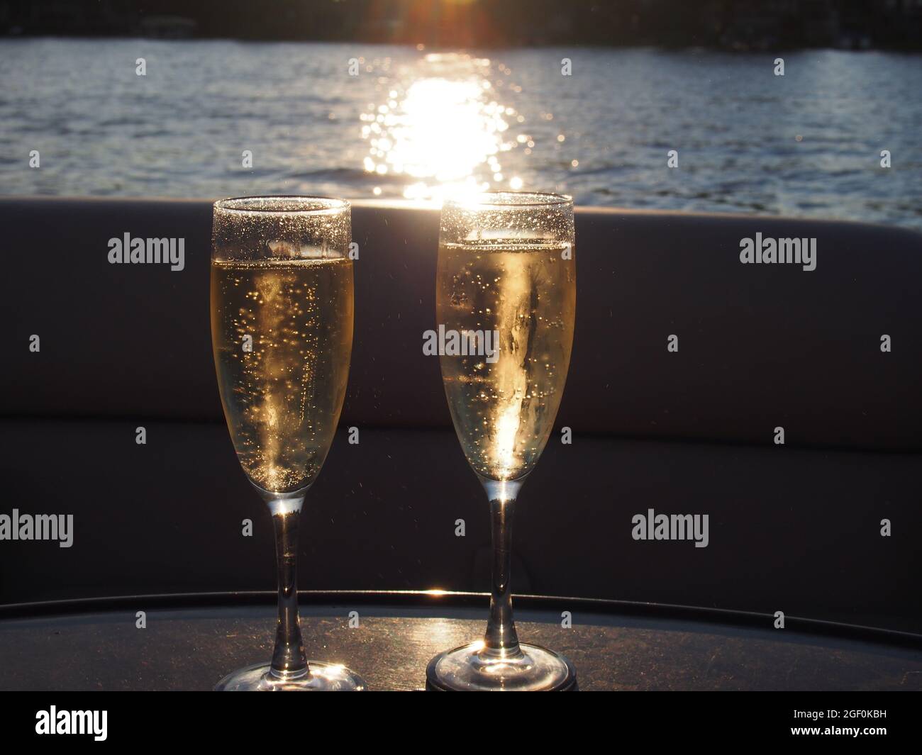 Tostada con champán y burbujas con luz solar contra una puesta de sol en el lago Foto de stock