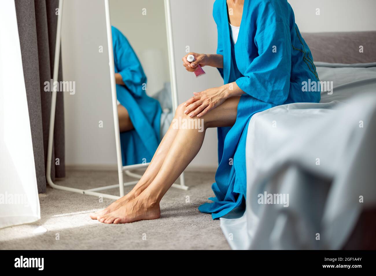 Mujer aplicando crema cosmética en las piernas Foto de stock