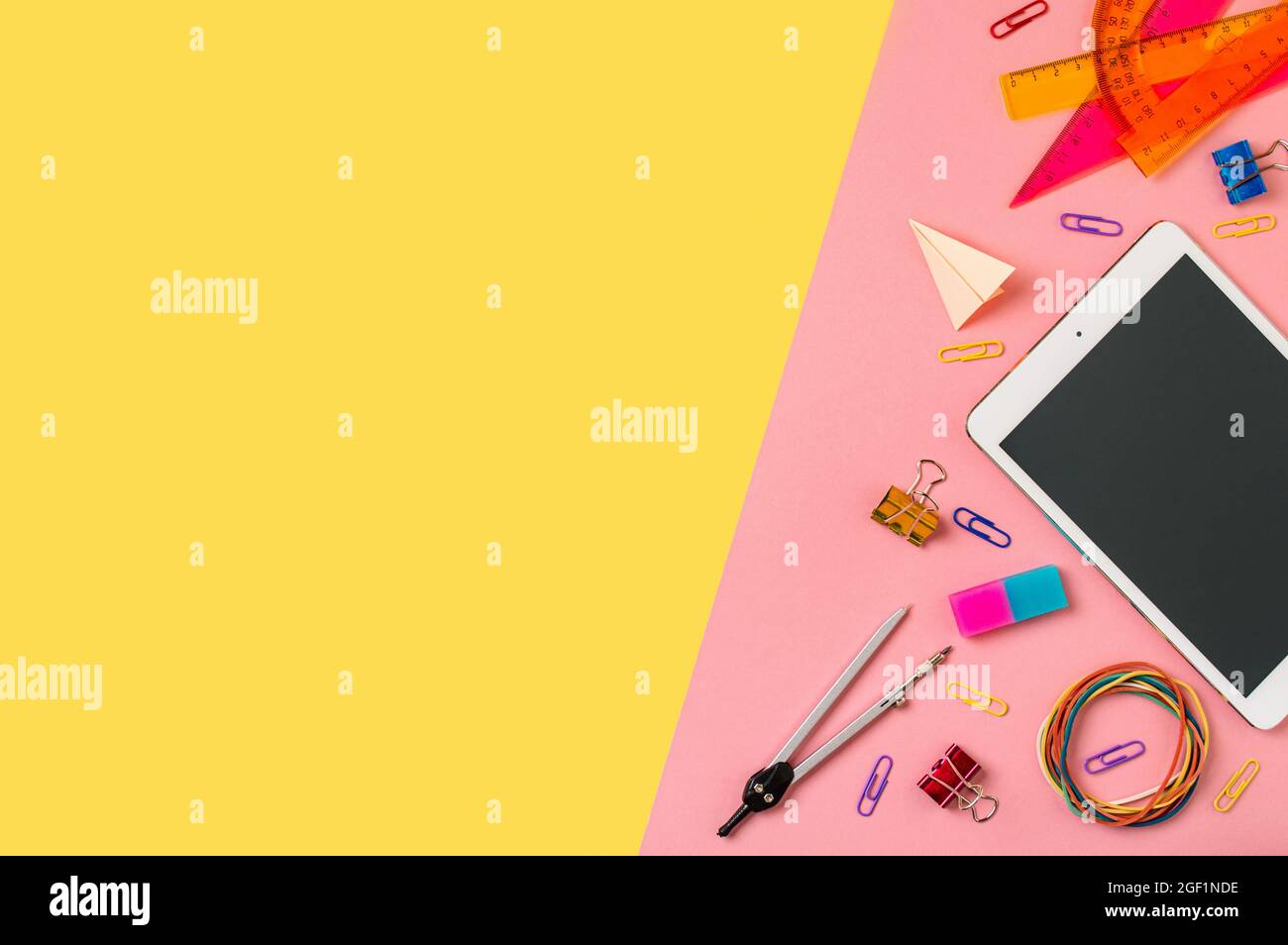 Creativo escritorio para estudiantes con tablet pc y coloridos materiales escolares modernos sobre fondo de duotono amarillo y rosa. Vista superior. Capa plana. Espacio de copia. Concepto de vuelta a la escuela Foto de stock