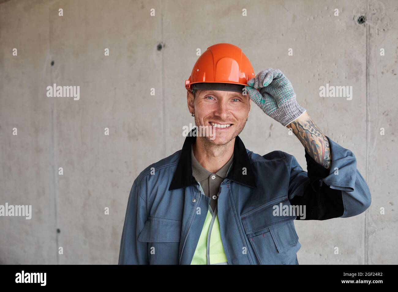 Retrato de trabajador de la construcción sonriente usando casco mientras  posaba contra la pared de hormigón, espacio de copia Fotografía de stock -  Alamy