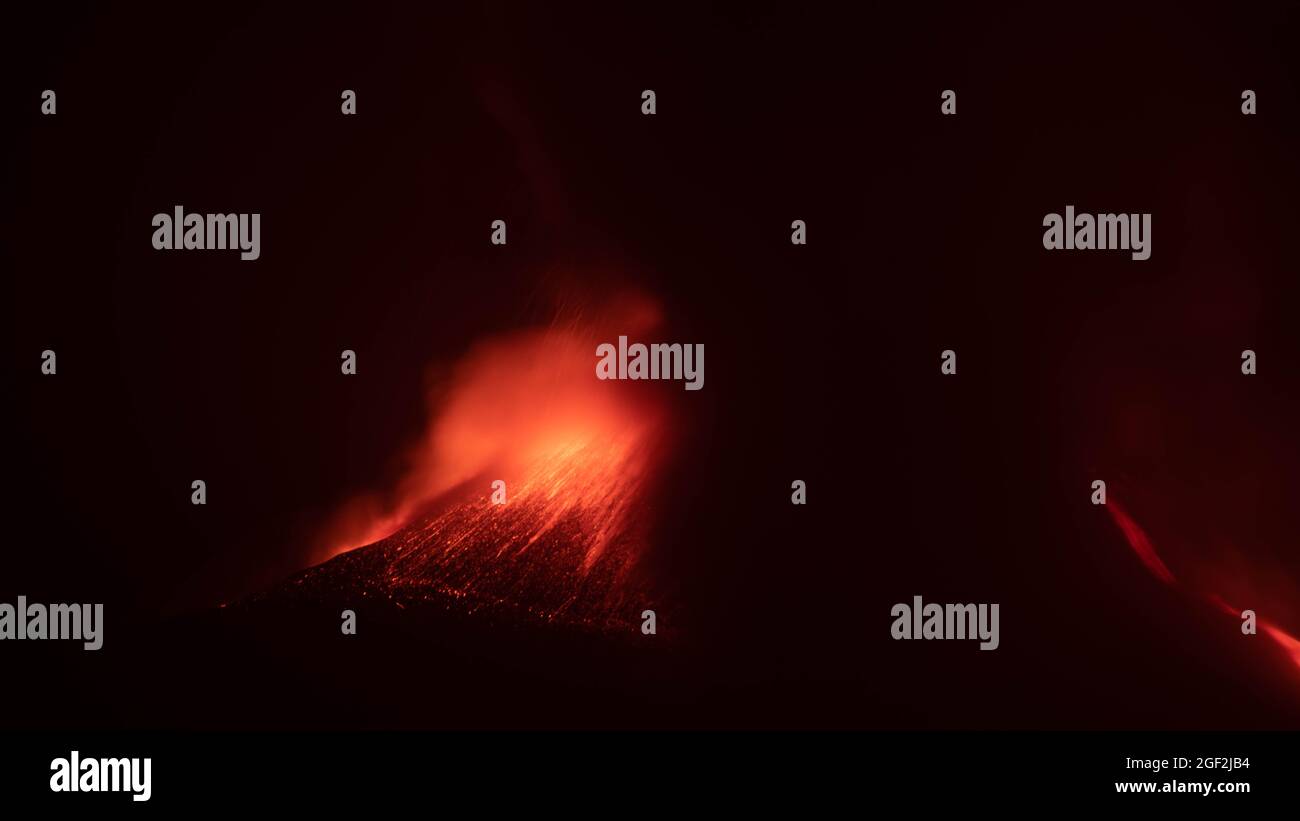 Erupción en el volcán Etna en Sicilia con explosiones de lava resplandeciente y humo por la noche. Foto de stock