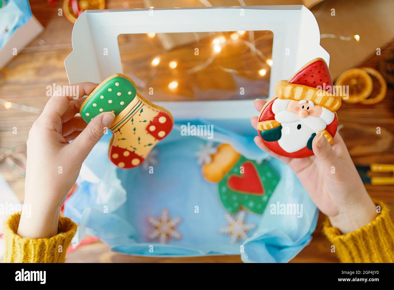 Las manos de la chica en jersey de punto sostienen el pan de jengibre de  Navidad con hielo. Galletas en forma de calcetín y Santa Claus. Caja de  regalo con papel y