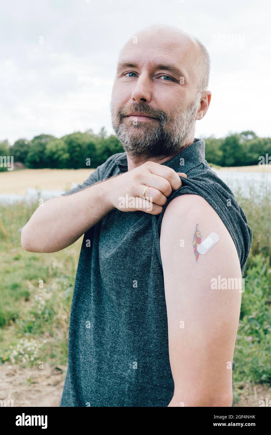 Hombre vacunado mostrando vendaje por tatuaje en el brazo Foto de stock