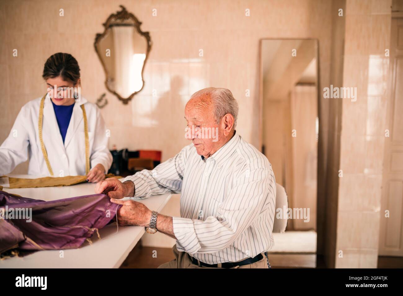 Fabricante de tocadores macho senior en funcionamiento que elimina las roscas de la tela en el taller Foto de stock