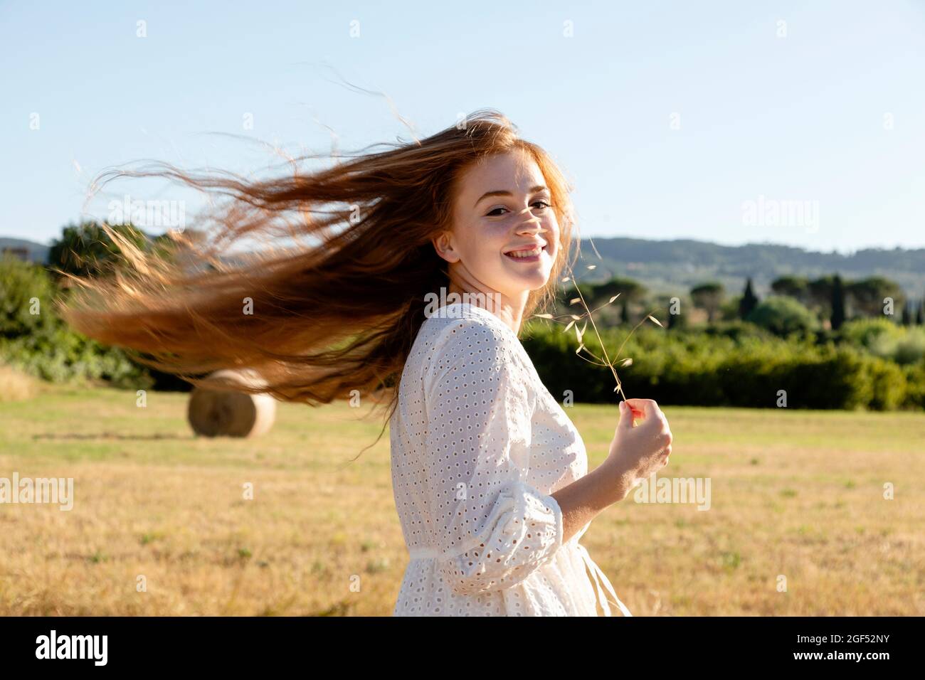 Mujer pelirroja con tallo de planta que sacude el cabello durante el día soleado Foto de stock