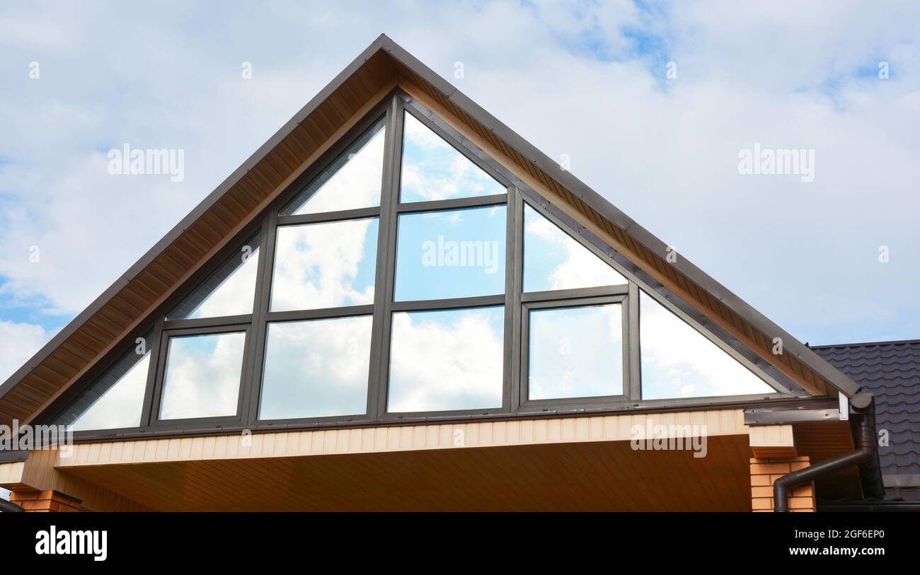 Un primer plano de una ventana panorámica del ático de una casa moderna,  diseño triangular de la ventana del ático, un gran tragaluz panorámico en  un techo de dos aguas Fotografía de