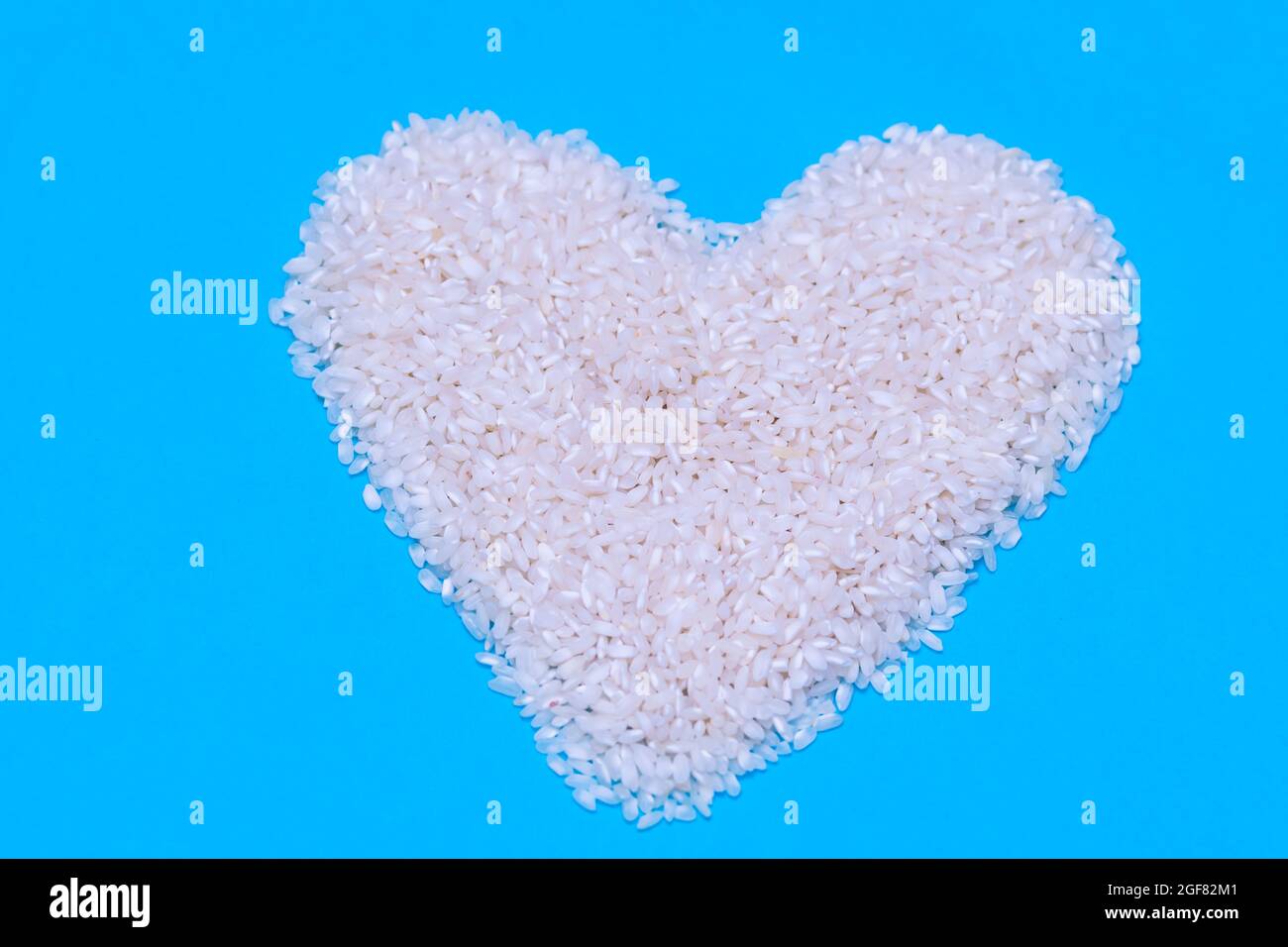 un puñado de arroz blanco crudo en forma de corazón sobre fondo azul. concepto de comida, cocina y vida saludable Foto de stock