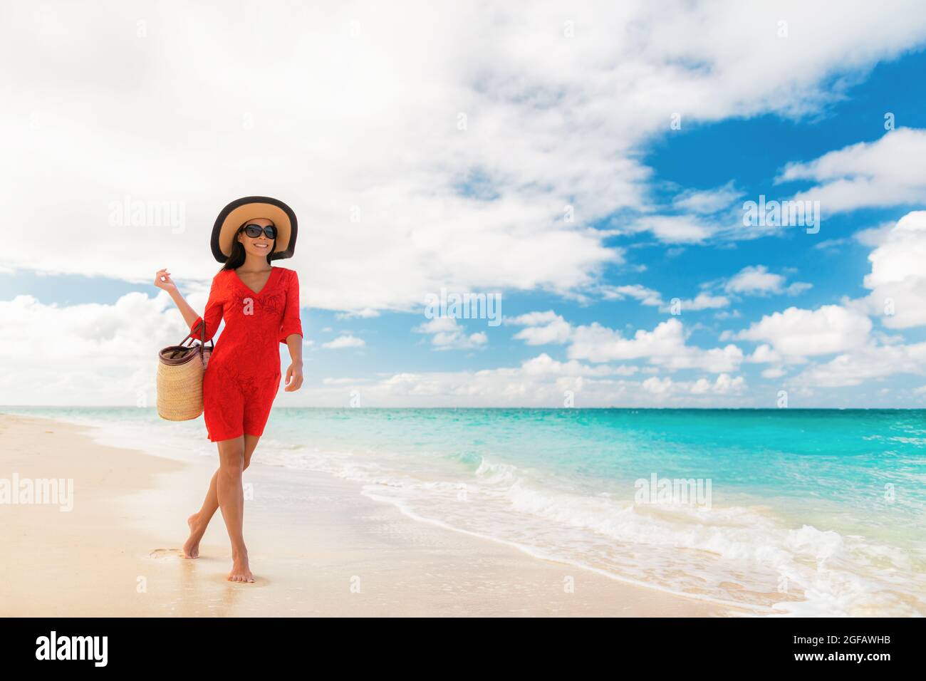 juez dirección grava Vacaciones de lujo en la playa elegante señora caminando relajándose en  vacaciones con accesorios de playa gafas de sol, sombrero y bolsa con ropa  de playa roja Fotografía de stock - Alamy