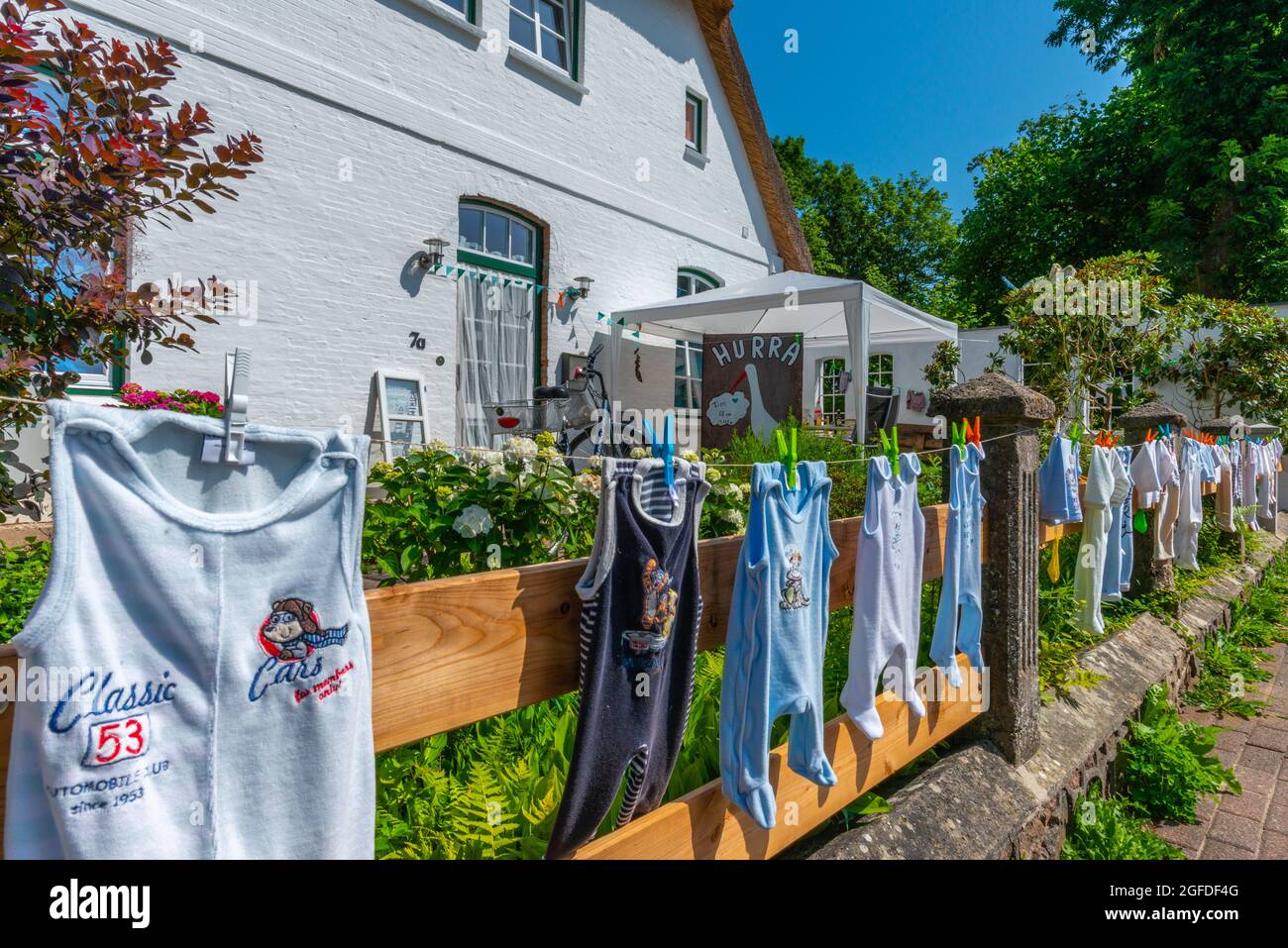 Colgando ropa de bebé en la línea de lavado en el jardín frontal es un antiguo traditon en la campiña, Süderstapel,Schleswig-Holstein, Norte de Alemania Foto de stock